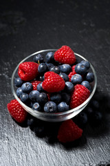 fresh berries in a glass bowl on dark background, vertical top view