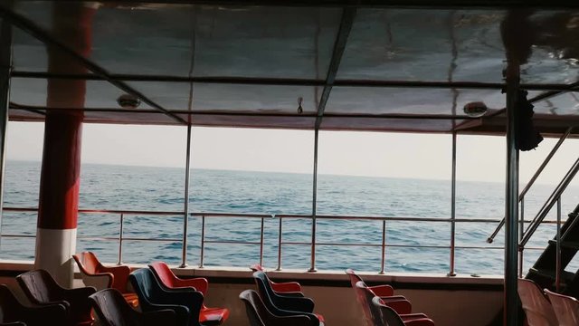 Camera is inside cruise yacht boat sailing in open sea rocking on big waves on clear sunny day with rows of empty seats.
