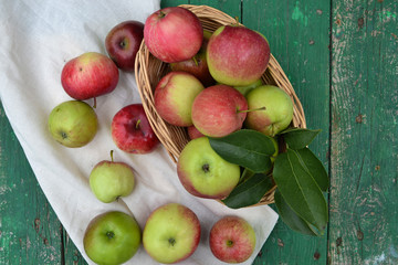 Fresh apples in basket on green wooden background. Harvest time. 