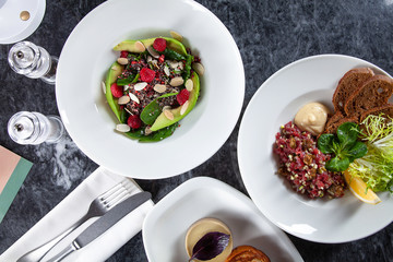 Top view on table with plenty of food. European and Middle Eastern cuisine. Food for breakfast. Tartare salad, sweet salad and toast on marble table. Set of dishes on table concept with copy space. 