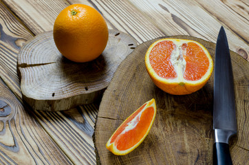 Sicilian oranges and knife with black knob rests on a wooden board, which stands on a wood table