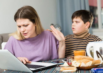 Young woman working at laptop and son trying to talking with she