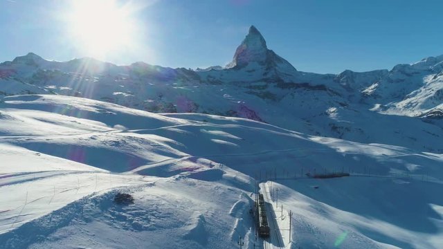 Matterhorn Mountain, Railway and Train in Sunny Winter Day. Swiss Alps. Switzerland. Aerial View. Reveal Shot. Drone Flies Backwards, Camera Tilts Up