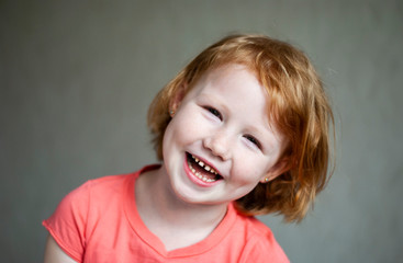 Studio shot of cute happy and emotive young redhead girl in pink t-shirt smiling feeling happiness.