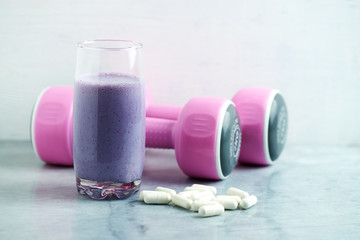 Glass of Protein Shake with milk and blueberries. Creatine capsules and pink dumbbells in background. Sport nutrition. Stone / Wooden background. Copy space. 
