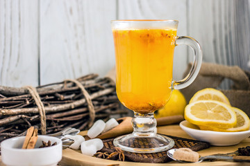  Green tea with sea buckthorn and ginger in a glass mug with a handle. Vitamin tea of ​​yellow color with berries, cinnamon, lemon, spices and ginger in a transparent mug on a gray background.