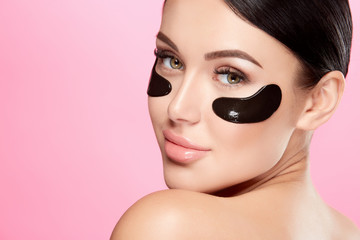 Young girl with nude make up and naked shoulders at studio background,black eye patches on face, beauty photo concept.