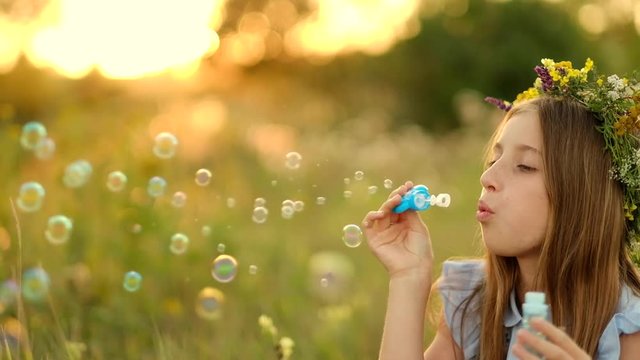 Girl is blowing bubbles on the meadow and during sunset