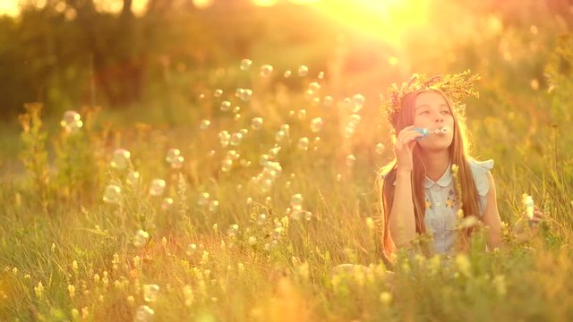 Girl is blowing bubbles on the meadow and during sunset