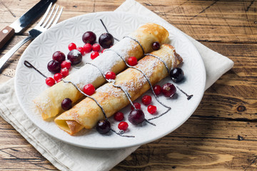 Pancakes tube with chocolate and berries on a plate. Wooden background.