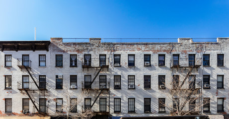 Old white brick apartment building with windows and fire escapes and an empty blue sky background...