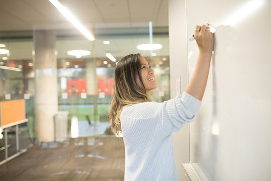Side view of young businesswoman writing on white board in office