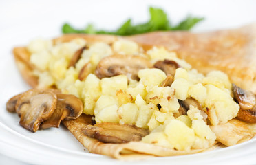 Thin delicious pancake with potatoes and mushrooms on white
