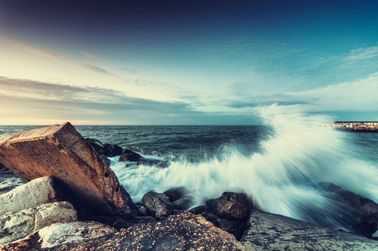 Onda del mare si infrange sugli scogli al tramonto