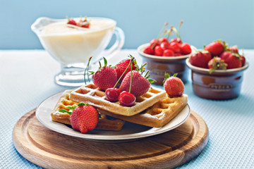 Breakfast. Viennese waffles with strawberries and cherries and cream on a white plate on a light background