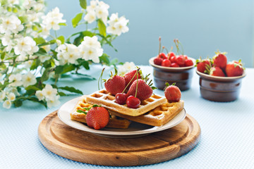 Breakfast. Viennese waffles with strawberries and cherries on a wooden board on a light background. Spring breakfast