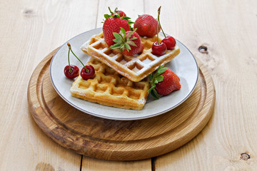 Breakfast. Viennese waffles with strawberries and cherries on a wooden board on a light background. Spring breakfast