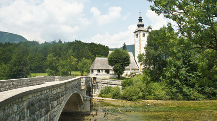 Fototapeta na wymiar Scenic view of the Church of St. John the Baptist, Julian Alps and bridge, Bohinj, Slovenia