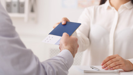 Travel agent giving passport with tickets to tourist