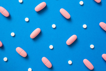 White and pink pills on blue background top view for text