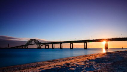 Bridge over glassy smooth water just after sunset, as the last light of the day burns on the horizon. Fire Island Inlet Bridge - Long Island New York.  - obrazy, fototapety, plakaty