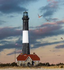 Closeup of an old lighthouse and American Flag in front of large puffy clouds getting lit up with...