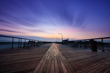 Fototapeta na wymiar Moody empty boardwalk at dusk. Dramatic scene with blue tones and wispy sweeping clouds 