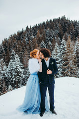 A pretty couple go to the winter pine forest, a woman in a blue wedding dress, a man in a suit