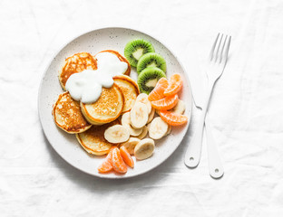 Delicious breakfast or snack - pancakes with fruit and sour cream on a light background, top view. Baby food