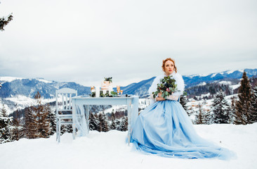 A charming bride in a blue dress with bouquet in hands sitting on a chair against a background of...