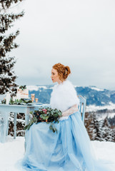Glorious red-haired girl with a bouquet in her hands sitting on a chair against the backdrop of winter mountains