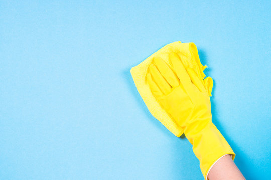 Hand In Yellow Gloves  And Microfiber Rag Cleaning Blue Background.