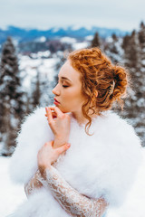 Portrait of a charming red-haired girl against the background of the winter mountains.