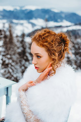 Portrait of a gorgeous red-haired girl against the background of the winter mountains.