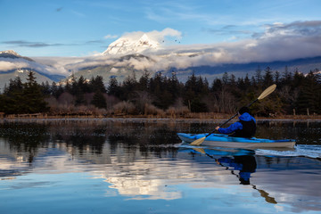 Adventurous man kayaking in peaceful water during a cloudy winter day. Taken in Squamish, North of...