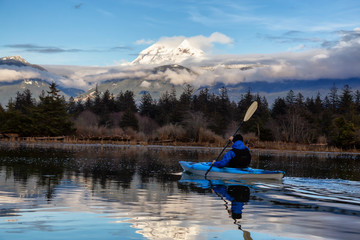 Adventurous man kayaking in peaceful water during a cloudy winter day. Taken in Squamish, North of...