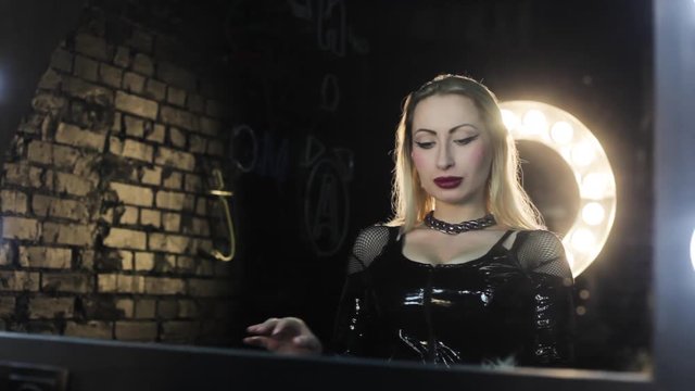 Woman with a BDSM whip looks in the mirror at herself.