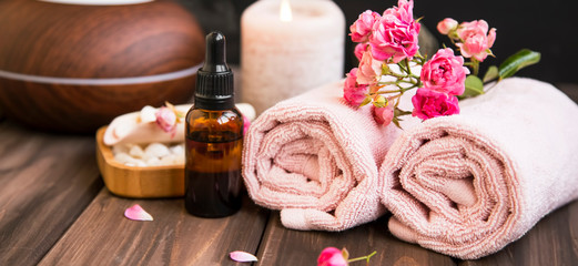 Obraz na płótnie Canvas Spa still life with towels, rose oil bottle, rose flowers on wooden background, spa and wellness setting