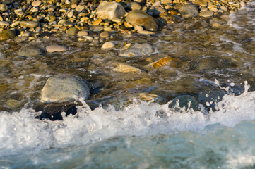 pebble stones on the sea beach, the rolling waves of the sea with foam