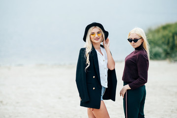 Two pretty girls blondes in glasses walking along the coast, talking and enjoying life.