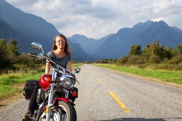 Woman riding a motorcycle on a scenic road surrounded by Canadian Mountains. Taken in Pitt Meadows, Greater Vancouver, BC, Canada.