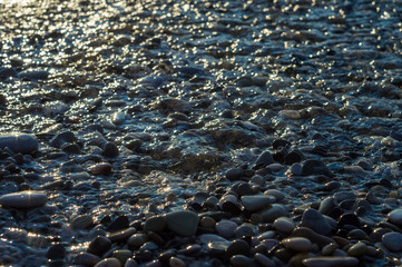 pebble stones on the sea beach, the rolling waves of the sea with foam