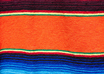 Obraz premium Multicolored cotton blanket with southwestern patterns from a market in Santa Fe, New Mexico, USA. One primary orange band in middle, other smaller bands are yellow and green and blue.