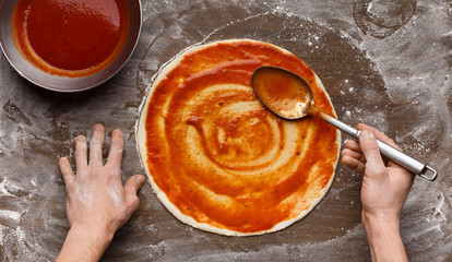 Man adding tomato sauce to italian pizza base