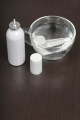 Inhaler for the treatment of respiratory organs. Spray can and cap white. The tip is soaked in water from drying. On a dark surface.