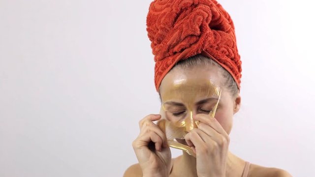 Close-up of a woman removing a golden mask from her face. Clear skin