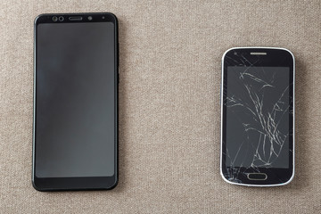 Comparison of two black mobile phones, old cellphone with cracked screen and new modern on light cloth copy space background. Technology progress and replacement concept.