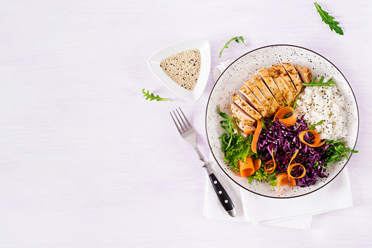 Healthy salad. Buddha bowl dish with chicken fillet, rice,  red cabbage, carrot, fresh lettuce salad and sesame. Healthy balanced eating. Top view.