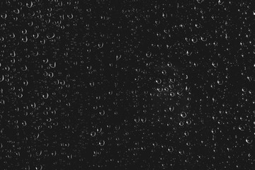 Dirty window glass with drops of rain. Atmospheric monochrome dark background with raindrops. Droplets and stains close up. Detailed transparent texture in macro with copy space. Night rainy weather.