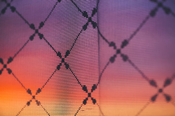 Amazing romantic sunset in window behind silhouettes of tulle texture. Wonderful pink orange violet dawn sky from window through patterned curtain. Cosiness background of scenic sunrise. Copy space.